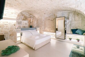 A bedroom with a stone wall, a bed, a bedside table, a mirror, and a window.