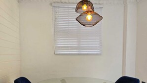 Un comedor con una mesa redonda de vidrio, dos sillas azules y una lámpara colgante.