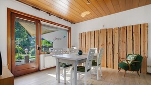 Een eethoek met een tafel en stoelen, een houten wand en een uitzicht door een glazen deur.