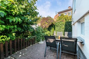 Een terras met een tafel en stoelen, omgeven door een houten hek en weelderige beplanting.