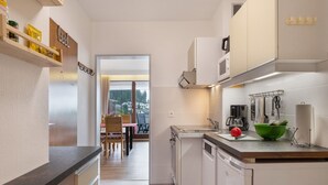 Une cuisine moderne avec des meubles blancs, un lave-vaisselle, un four à micro-ondes et un saladier vert posé sur le plan de travail.
