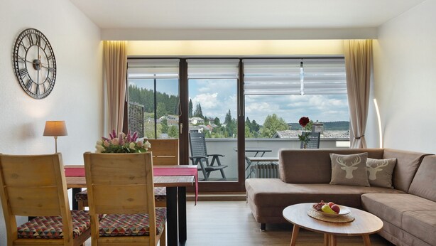 Un salon moderne avec un canapé, des fauteuils, une table, une horloge et une vue sur l’extérieur.