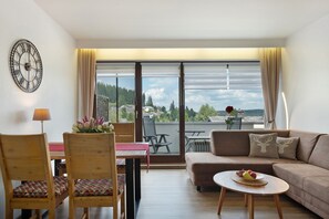 En moderne stue med sofa, stole, et bord, et ur og udsigt til det fri.