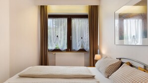 Une chambre d’hôtel avec un lit, une fenêtre avec des rideaux, un radiateur et une lampe fixée au mur.