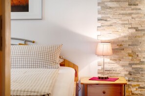 Un dormitorio con cama, mesita de noche con lámpara, cuadro en la pared y pared de piedra.