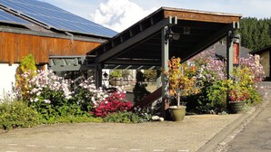 Un bâtiment à l’extérieur en bois, doté d’un espace extérieur couvert agrémenté de plantes en pot et de panneaux solaires sur le toit.