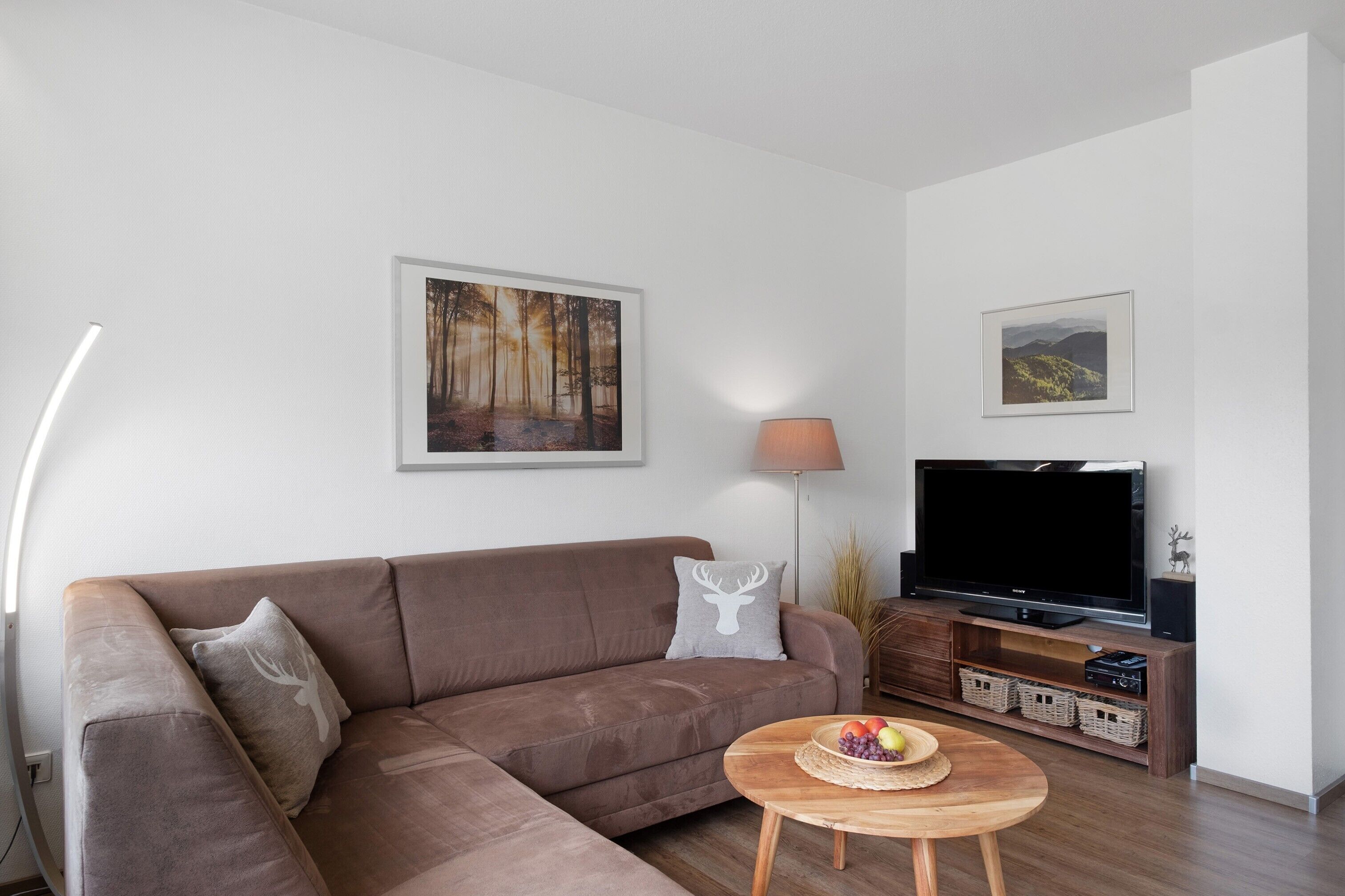 Ein modernes Wohnzimmer mit einer Couch, einem Flachbildfernseher, einer Lampe und einem Gemälde an der Wand.