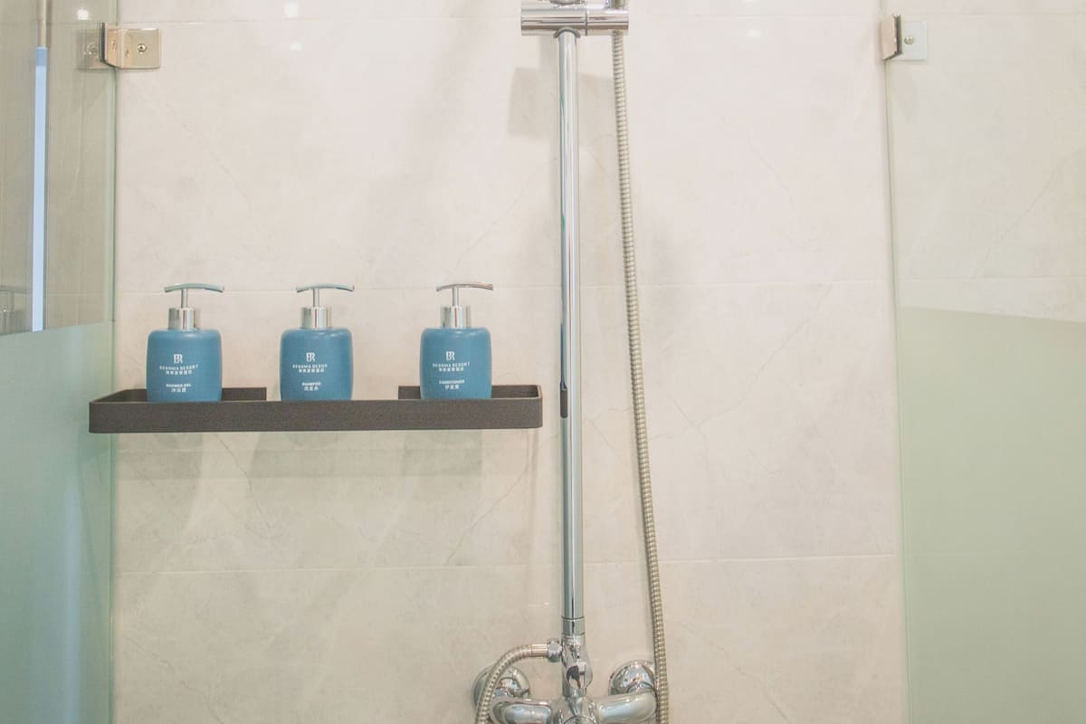 A shower with a handheld showerhead and a wall-mounted faucet. There are three blue bottles on a shelf below.