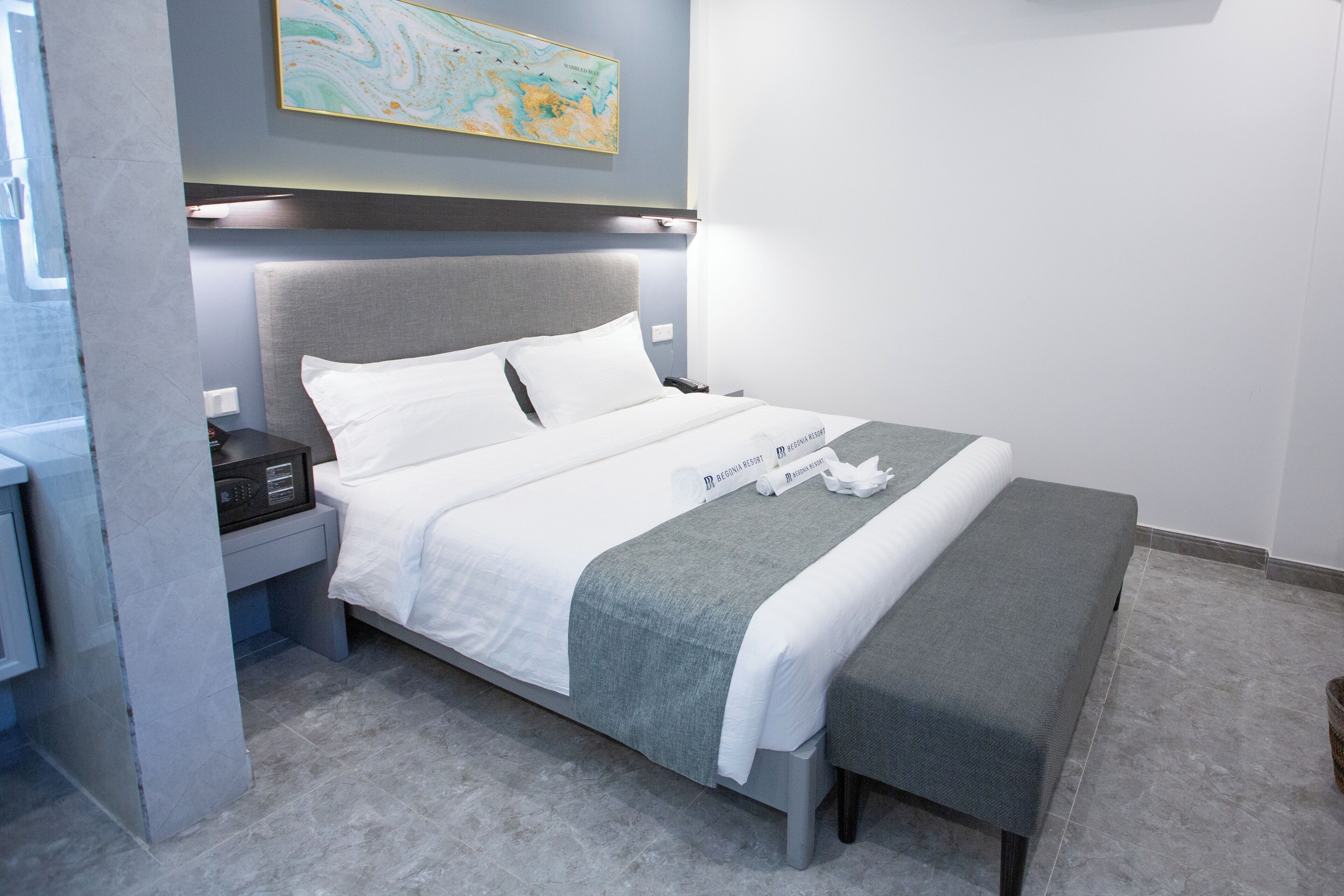 Ein modernes Hotelzimmer mit einem ordentlich bezogenen Bett, einem Nachttisch mit Lampe sowie einer Karte an der Wand.
