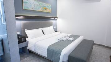 Ein modernes Hotelzimmer mit einem ordentlich bezogenen Bett, einem Nachttisch mit Lampe sowie einer Karte an der Wand.
