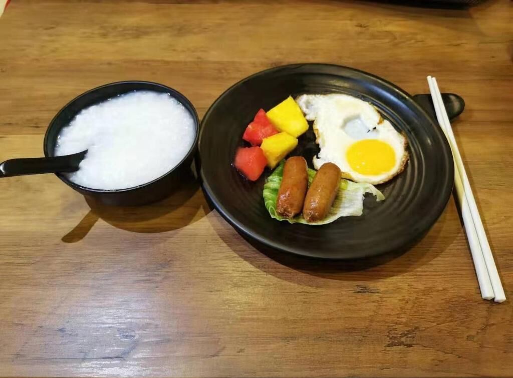 Una comida con un tazón de arroz y un plato de huevo frito, salchichas y verduras.
