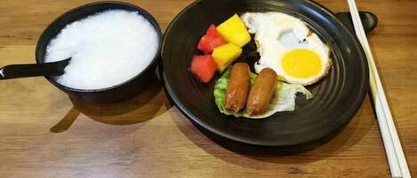 Una comida con un tazón de arroz y un plato de huevo frito, salchichas y verduras.