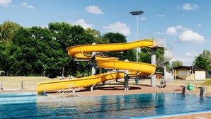 En swimmingpool med en gul vattenrutschkana och ett överbyggt område med trappor.