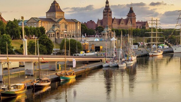 En hamn med flera båtar, en bro och historiska byggnader i bakgrunden.