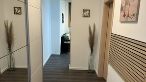 En hall med trägolv, en vägg täckt med speglar och två vaser med torkade växter.
