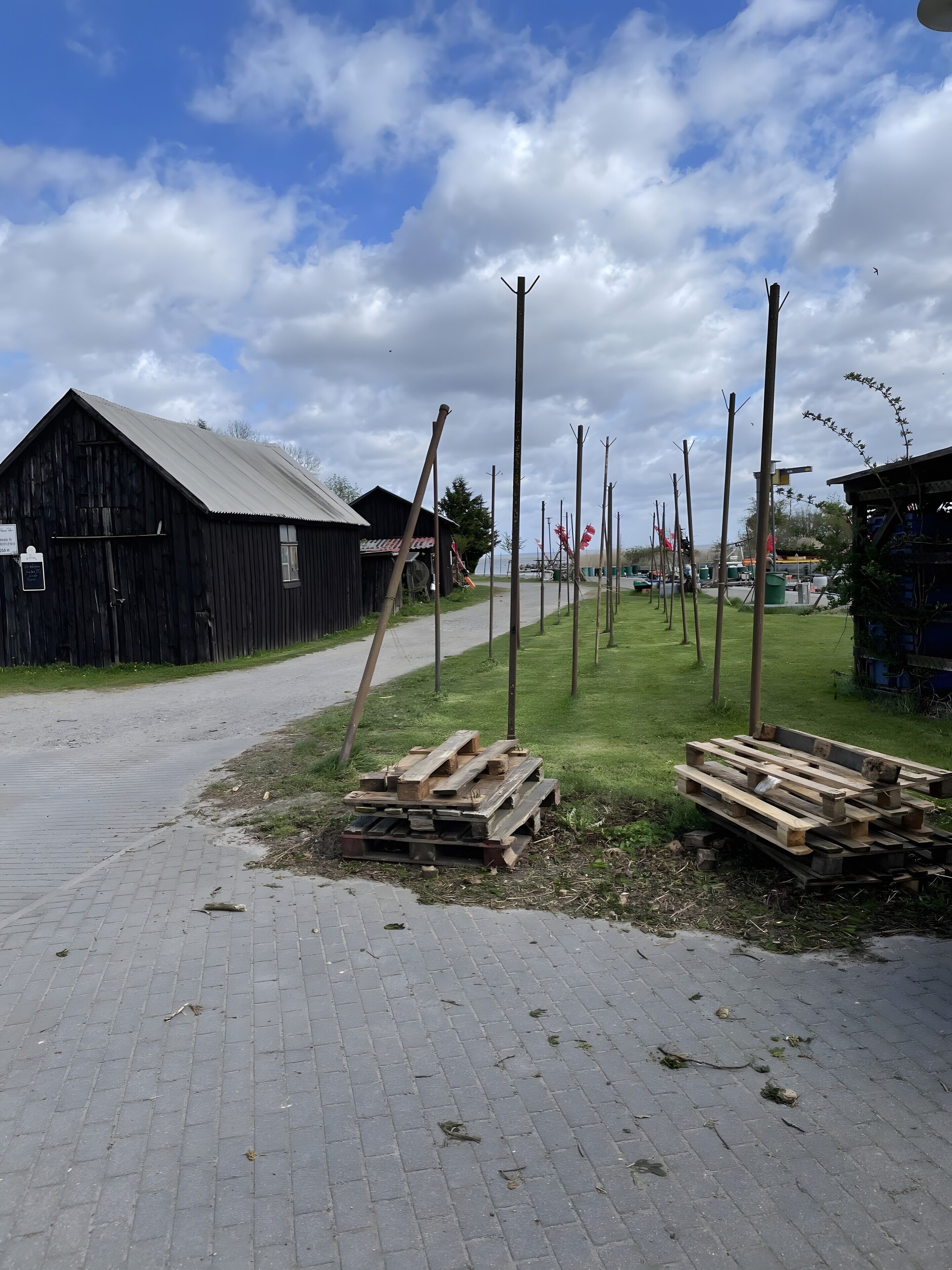 A rural setting with a paved road, wooden structures, and a grassy area.
