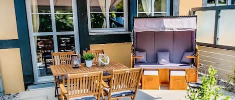 Un patio con mesa y sillas, un banco acolchado y un pequeño jardín.