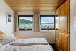 Een kamer met een bed, een houten kledingkast en een raam met uitzicht op groen.