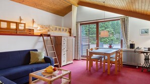 A cozy room with a blue sofa, wooden table, and a dining area with chairs. A ladder is leaning against a wardrobe, and a radiator is visible.