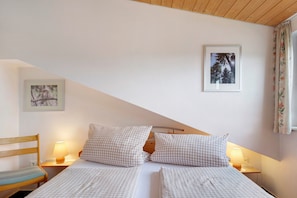 A bedroom with two beds, a wooden headboard, a nightstand with a lamp, and framed pictures on the wall. - Apartment 1 'Eule, 42qm' with Balcony and Wi-Fi (Schönwald im Schwarzwald)