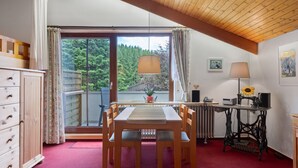 A room with a dining table, chairs, a radiator, a sewing machine, and a window with a view of trees.