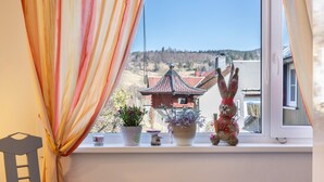 Une fenêtre donnant sur un immeuble, une petite étagère ornée d’objets décoratifs et un rideau.