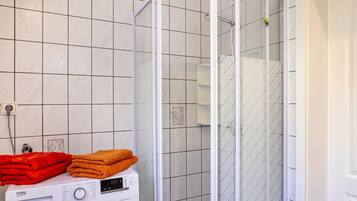 Un baño con lavadora, cabina de ducha de vidrio y paredes de azulejos.