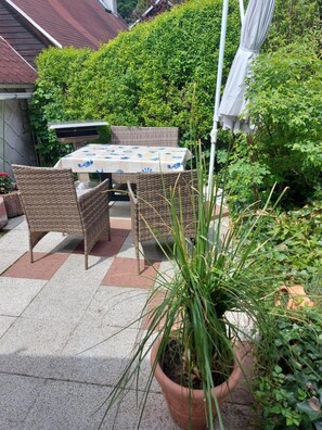 Een terras buiten met een tafel en stoelen, omringd door groen en een bloempot.
