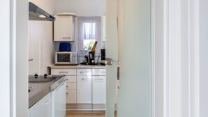 Une cuisine compacte avec des meubles blancs, un four à micro-ondes, une machine à café et une fenêtre ornée de rideaux légers.