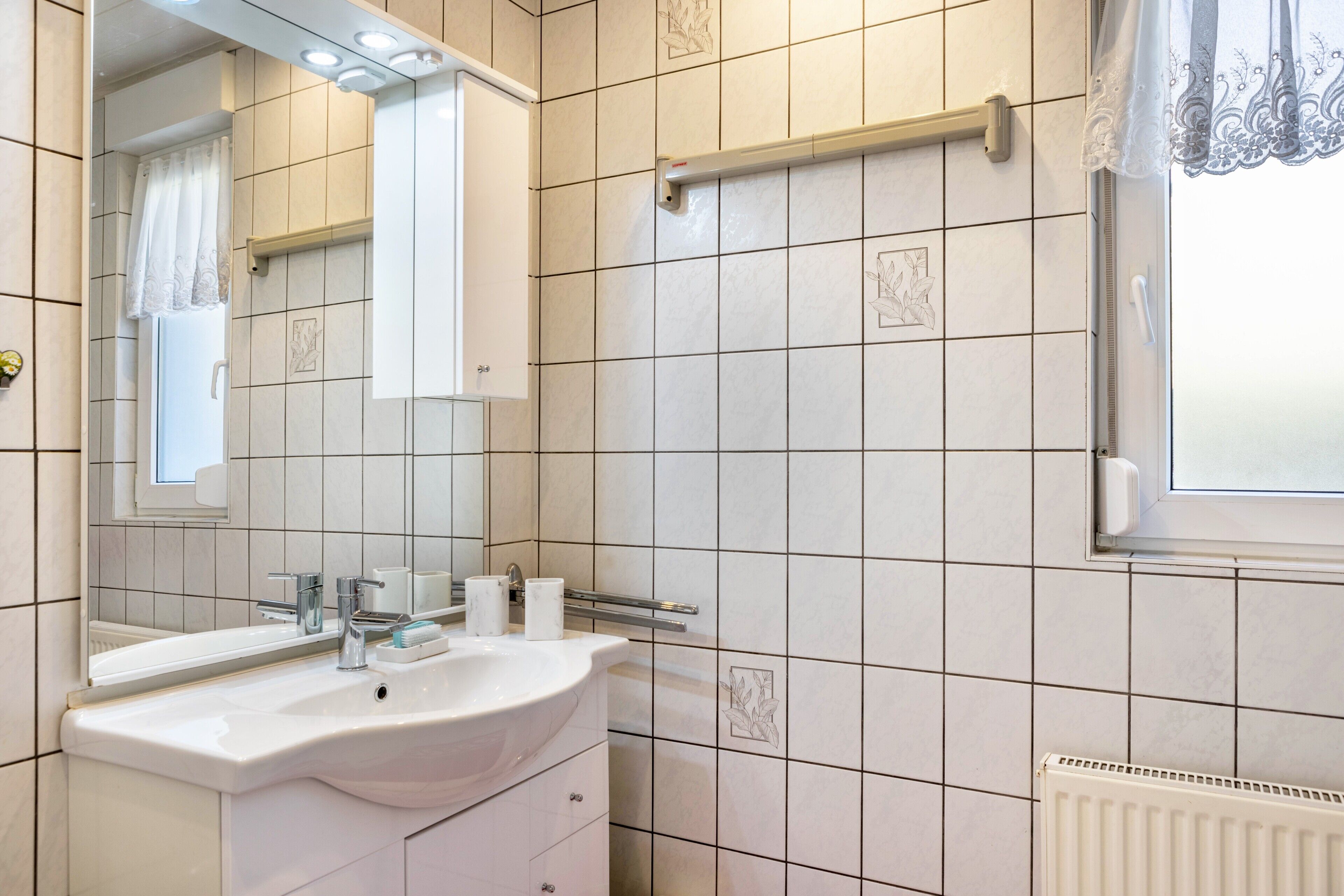 Ein Badezimmer mit weißem Waschbecken, Spiegel und gefliesten Wänden.