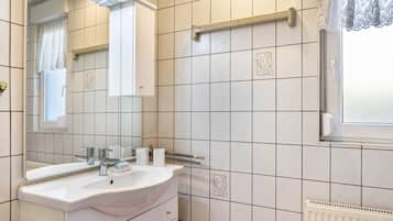 Ein Badezimmer mit weißem Waschbecken, Spiegel und gefliesten Wänden.