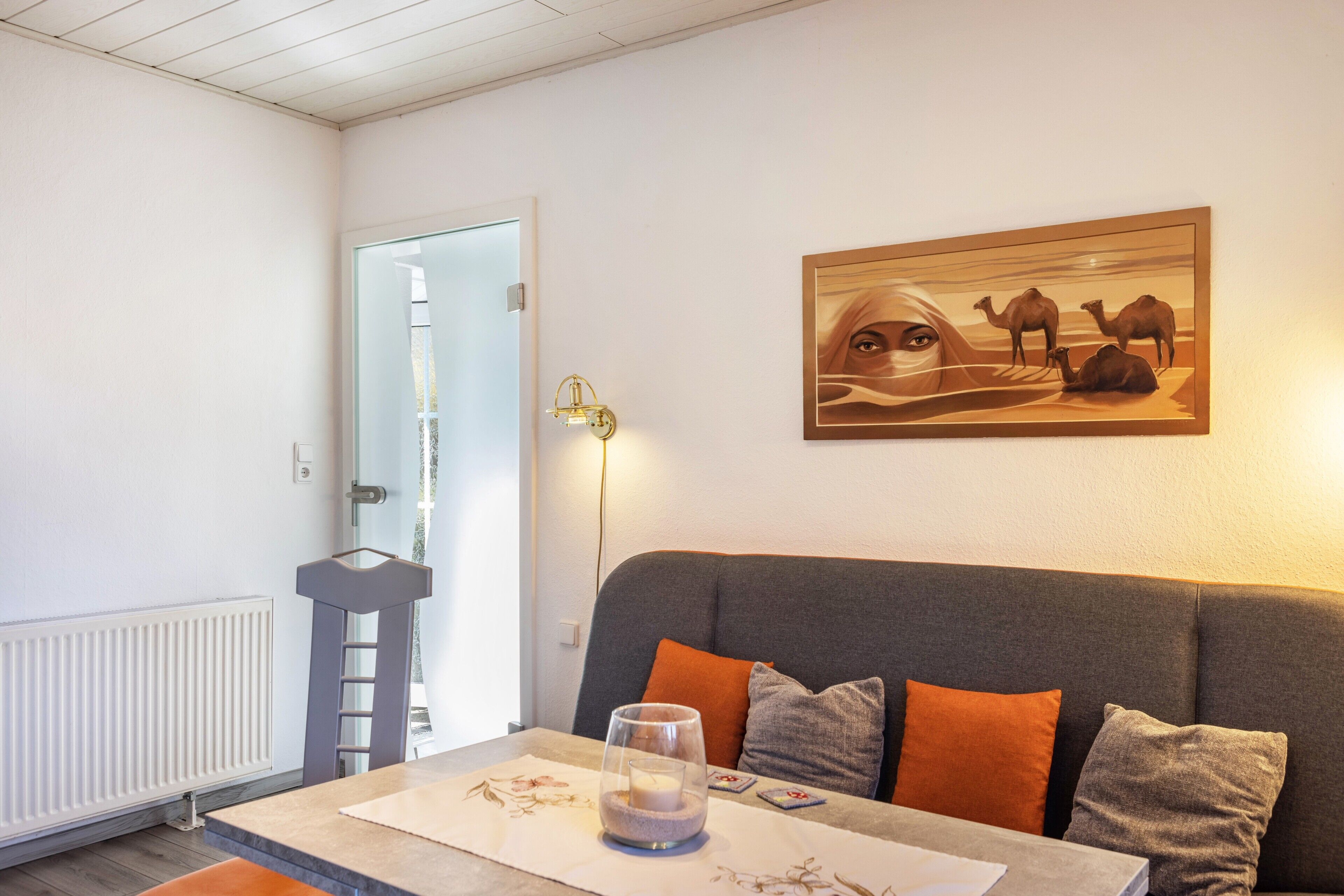 A living room with a sofa, a glass table with a candle, and a painting of camels on the wall.