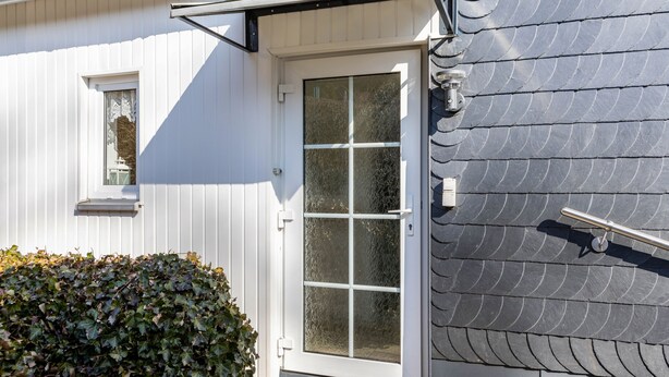 Une maison à l’extérieur blanc, avec un toit gris et une porte blanche dotée d’un panneau de verre.