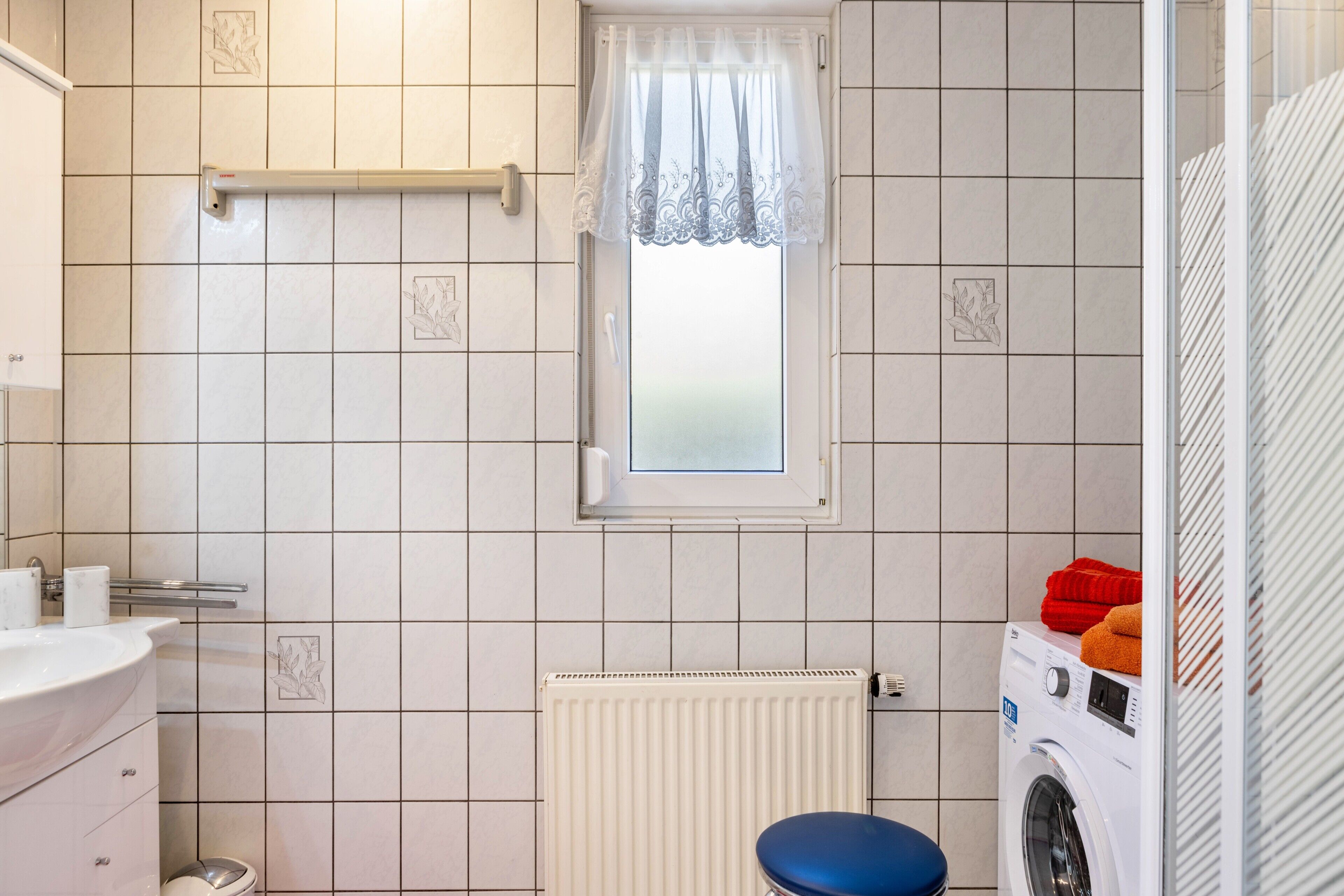 Ett badrum med handfat, toalett, fönster, element och tvättmaskin.