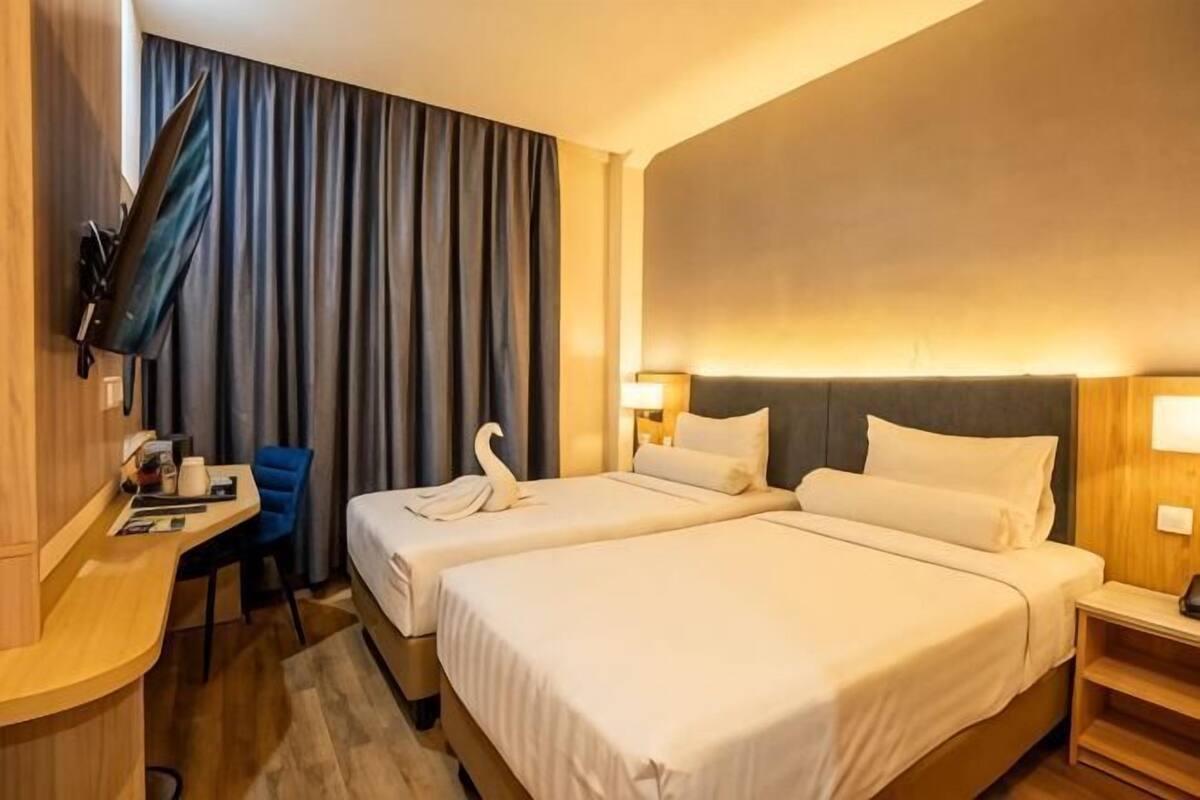 Une chambre d’hôtel avec deux lits, un bureau, une chaise, une télévision et une grande fenêtre avec des rideaux.