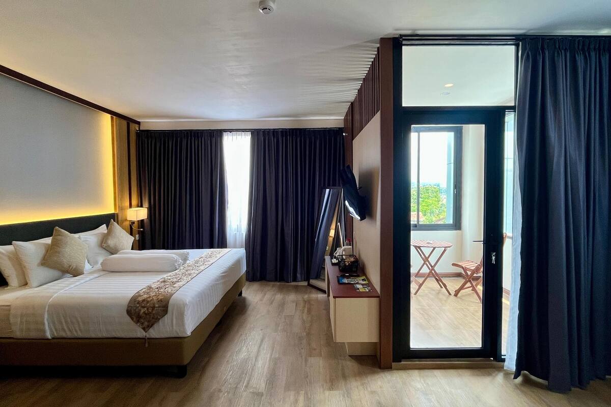 Une chambre d’hôtel avec un grand lit, un bureau, une chaise, un miroir et une porte coulissante donnant sur un balcon.