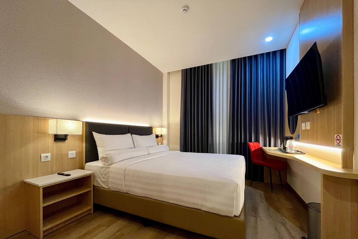 Une chambre d’hôtel comprenant un lit, une table de chevet, une lampe, une télévision et un bureau avec une chaise.
