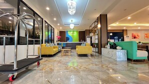 A hotel lobby with a reception desk, yellow sofas, a green sofa, a marble floor, and a chandelier. - Front One Boutique Adria Boyolali (Boyolali)