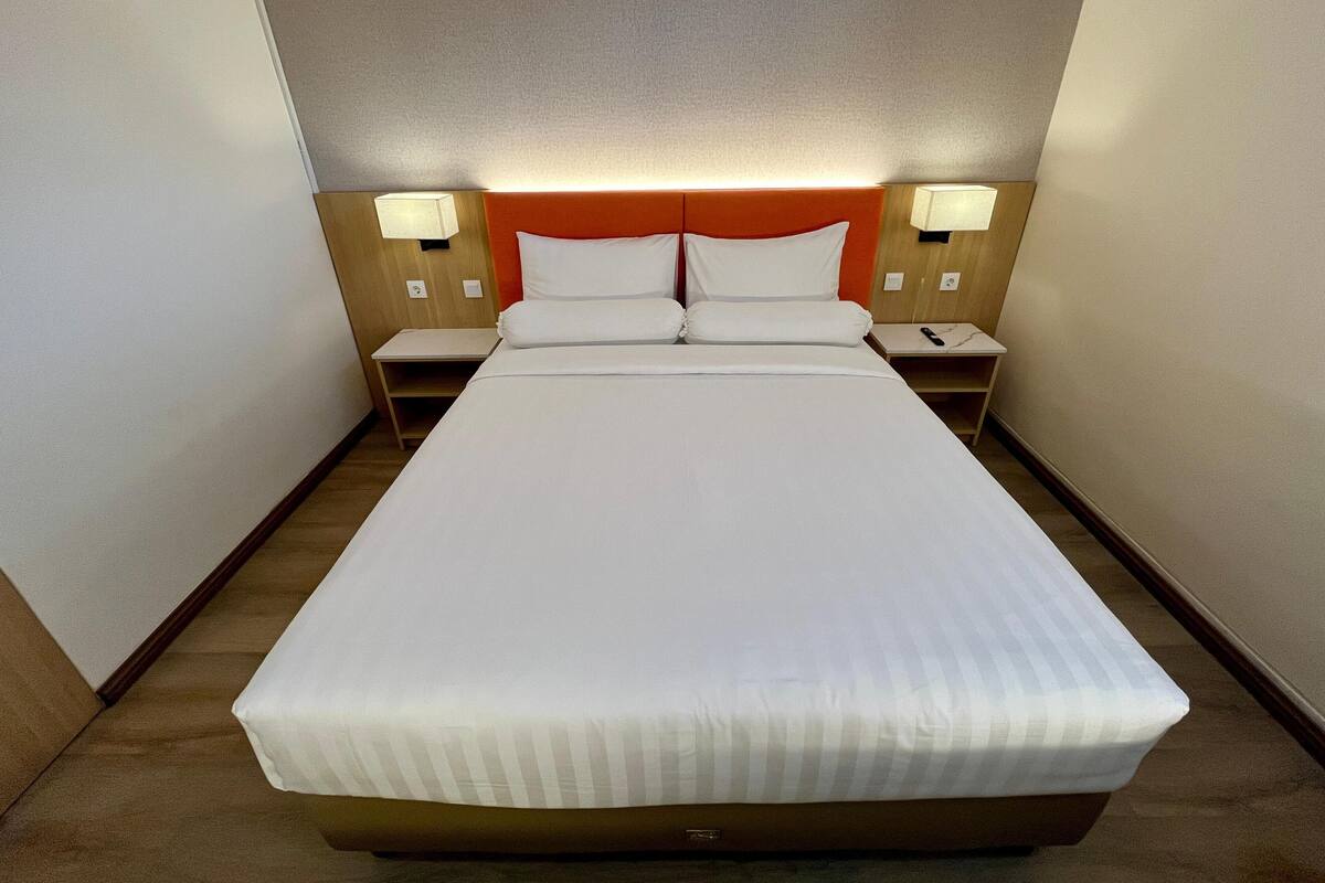 Une chambre d’hôtel avec un grand lit, deux tables de chevet et deux lampes fixées au mur.