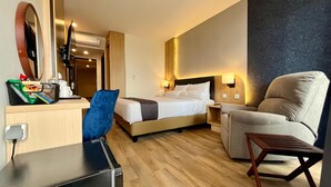 A hotel room with a bed, a desk with a chair, a small table, and a wall-mounted lamp. - Front One Boutique Adria Boyolali (Boyolali)