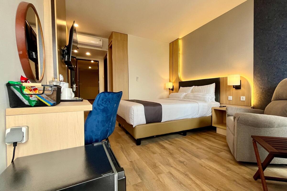Une chambre d’hôtel comprenant un lit, un bureau avec une chaise, une petite table et une lampe fixée au mur.