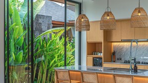 A modern kitchen with wooden cabinets, a large island with a sink, and hanging wicker pendant lights. - Rosita Ubud - Stunning 5BR Villa  (Ubud)