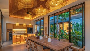 A modern kitchen with a wooden island, large windows, and tropical plants. - Rosita Ubud - Stunning 5BR Villa  (Ubud)