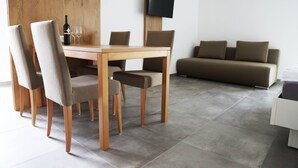 Un comedor moderno con una mesa y sillas de madera, un televisor montado en la pared y un sofá al fondo.