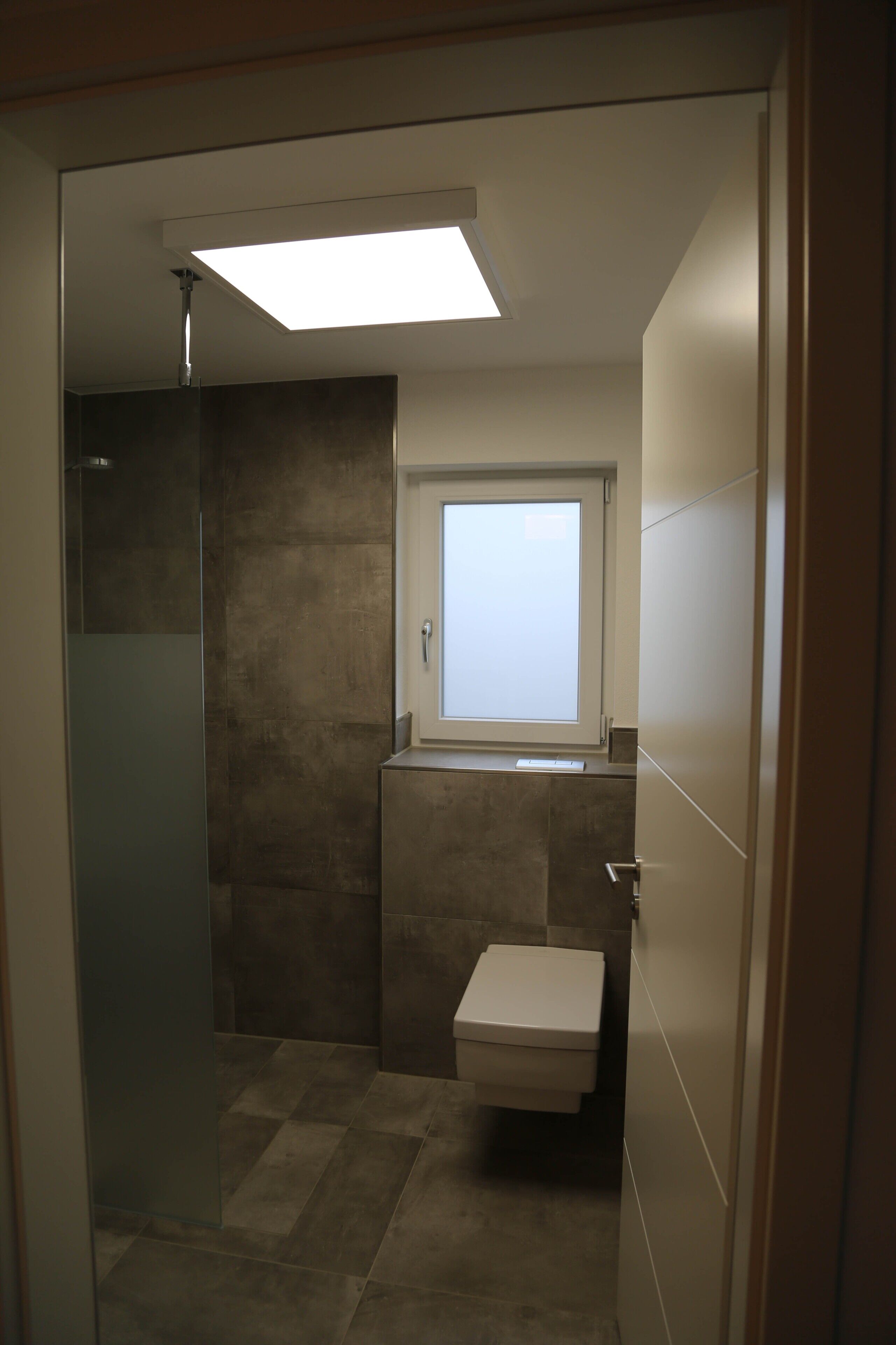 Een kleine badkamer met een douche, toilet en een raam.