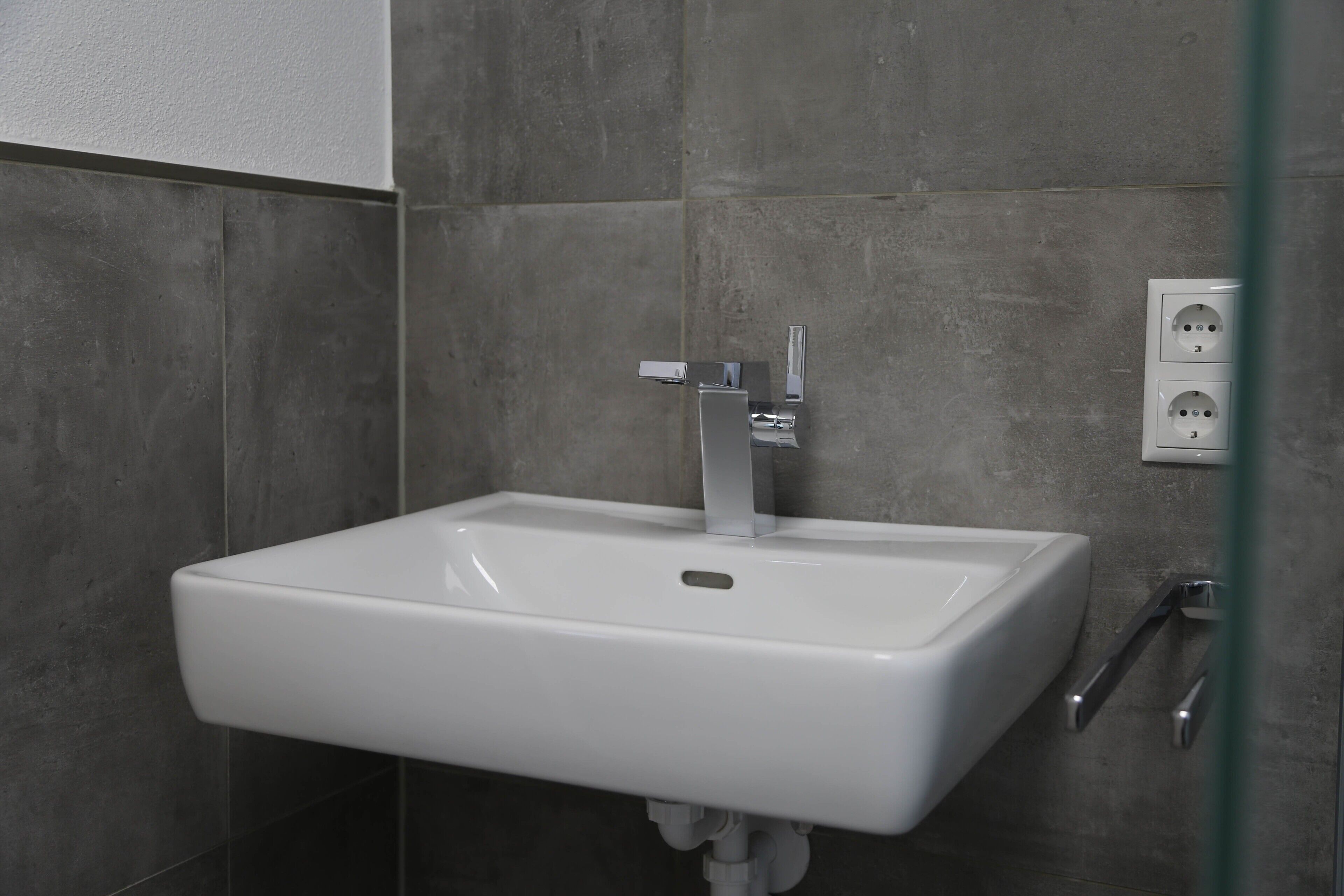 Une salle de bain avec un lavabo blanc, un miroir et une prise électrique murale.