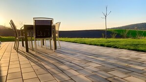 An outdoor seating area with a table and chairs, a paved walkway, and a view of a green field and hill in the background. - Apartment 'Nr 2' with Mountain View, Shared Terrace and Wi-Fi (Vaihingen)