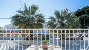 Una terraza con una mesa, sillas, una planta en maceta y vista al mar y palmeras.