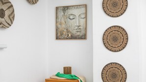 Una habitación con una mesita de noche de madera, un mantel verde y una obra de arte con el rostro de Buda en la pared.