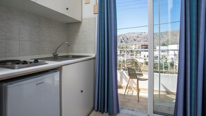 Una cocina moderna con refrigerador empotrado, un lavamanos y un ventanal con vistas a un balcón con una silla.